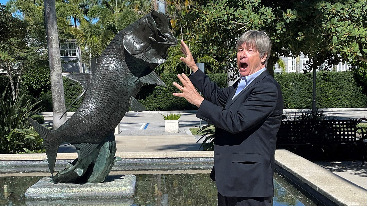 A man pretending that a fish statue is attacking him